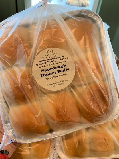 A square foil pan of browned sourdough dinner rolls are displayed in a bag to be sold at a local farmer's market.