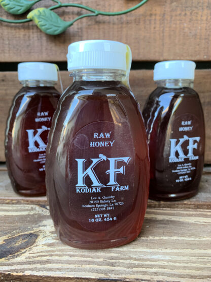 Three squeeze bottles of kodiak farm raw honey sit on a wood surface.