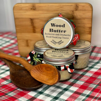 Small jars of wood butter sit stacked up beside two wooden spoons and a wood cutting board.